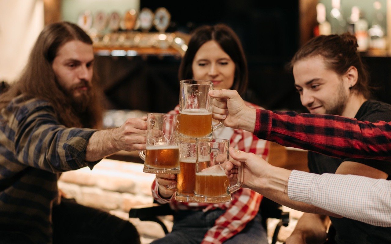 Symbolbild Bar mit separatem Raum: Freundesgruppe stößt mit Bier in warmer Bar an