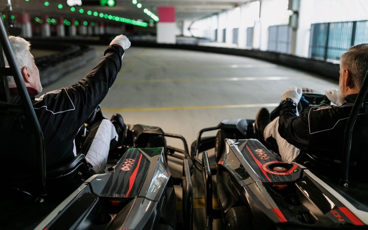 Symbolbild Kart: Zwei Erwachsene fahren Kart in der Halle, einer jubelt