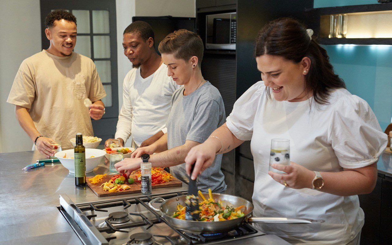 Symbolbild Kochkurs: Vier Erwachsene kochen lachend zusammen in einer Küche