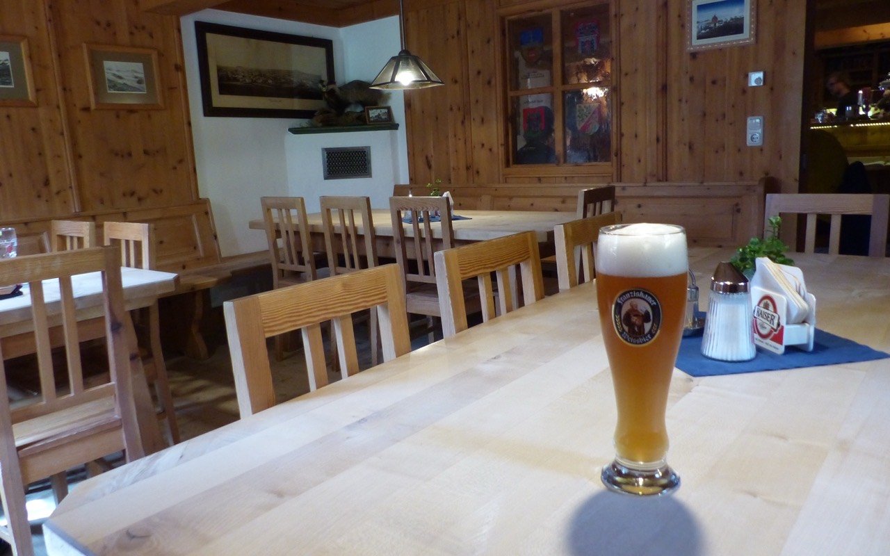 Symbolbild Restaurant mit Gruppenbereich: Gaststube mit Weißbierglas auf dem Holztisch