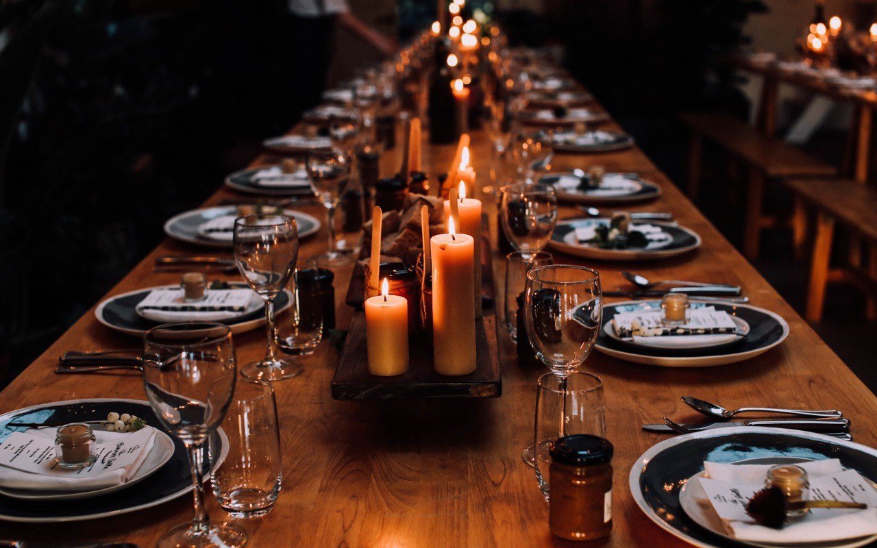 Symbolbild Restaurant mit Nebenräumen: Lange gedeckte Festtafel mit Kerzen in warmem Licht