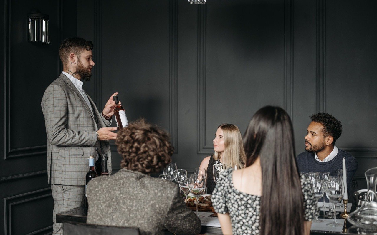 Symbolbild Eventlocation im Weinkeller: Sommelier präsentiert einer Gruppe Erwachsener Wein bei Verkostung